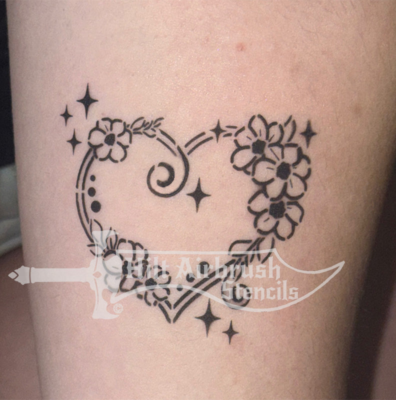 Heart-shaped tattoo with floral designs airbrushed on a person's arm, created with a Hilt Airbrush Stencil.