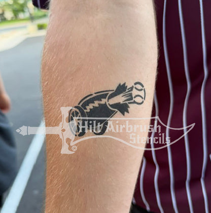 A temporary tattoo of a cannon shooting a baseball created by a stencil for baseball or softball airbrush tattoos.