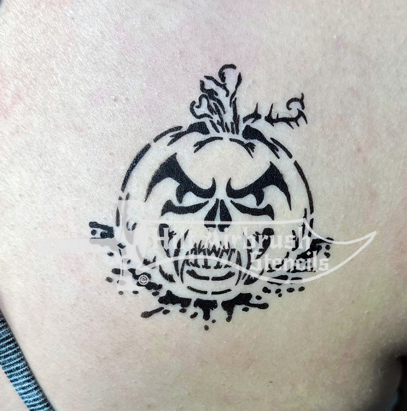 Black airbrush tattoo of a jack-o-lantern skull with decorative elements on a person's arm.