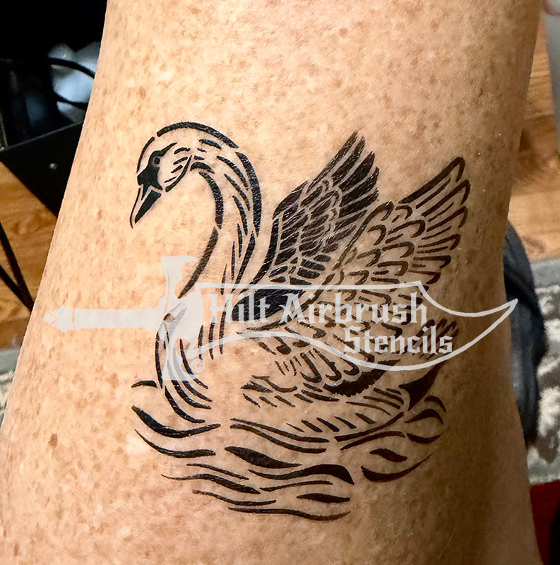 A black temporary airbrush tattoo of a swan with wings spread, applied to human skin. 