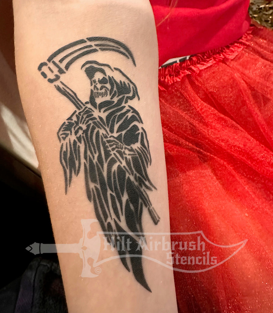 Airbrush tattoo of a Grim Reaper skeleton with a scythe, sprayed on a person's arm using a stencil from Hilt Airbrush Stencils.