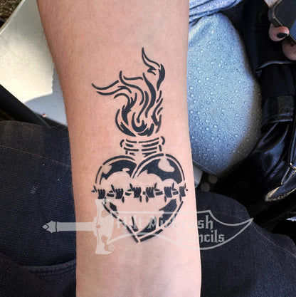 Airbrush tattoo of a heart with a flames and barb wire sprayed on a person's arm, using a stencil from Hilt Airbrush Stencils.