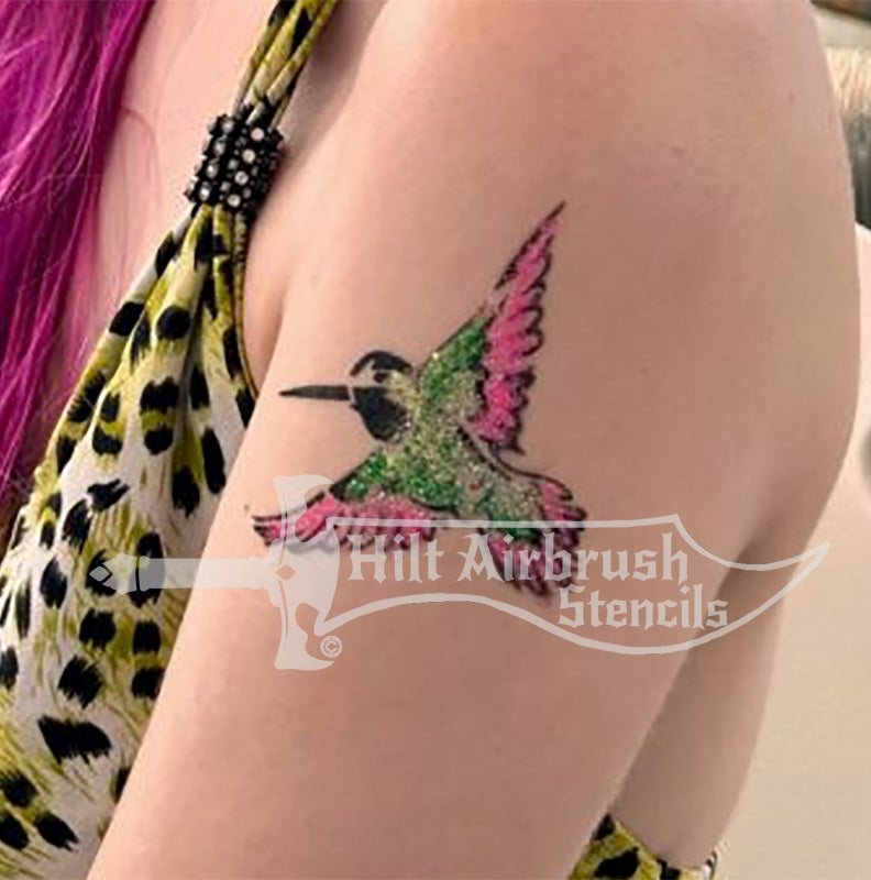 Colorful hummingbird tattoo airbrushed on a person's arm using a stencil from Hilt Airbrush Stencils.