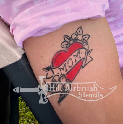 Airbrush tattoo of a heart with 'Mom' and bird on a person's arm, created with a Hilt Airbrush Stencils tattoo stencil.