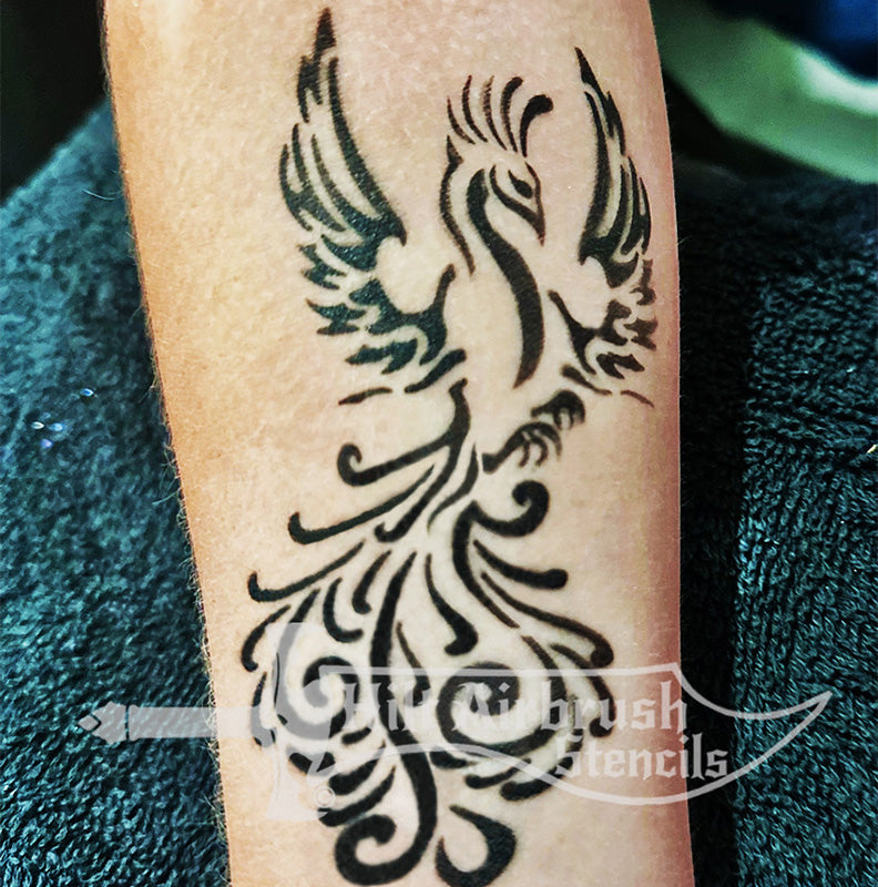Black tribal style phoenix tattoo on a person's arm designed by Hilt Airbrush Stencils.