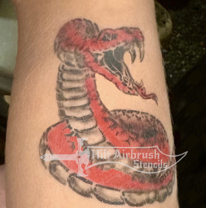 Airbrush tattoo of striking rattlesnake on a person's arm created with a tattoo stencil from Hilt Airbrush Stencils.